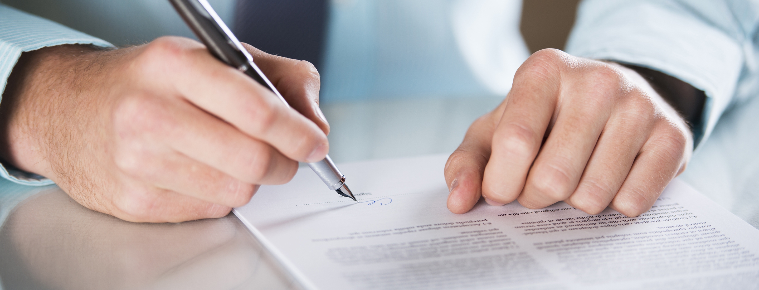 2880x1100 of a businessman’s hands signing a contract on a table