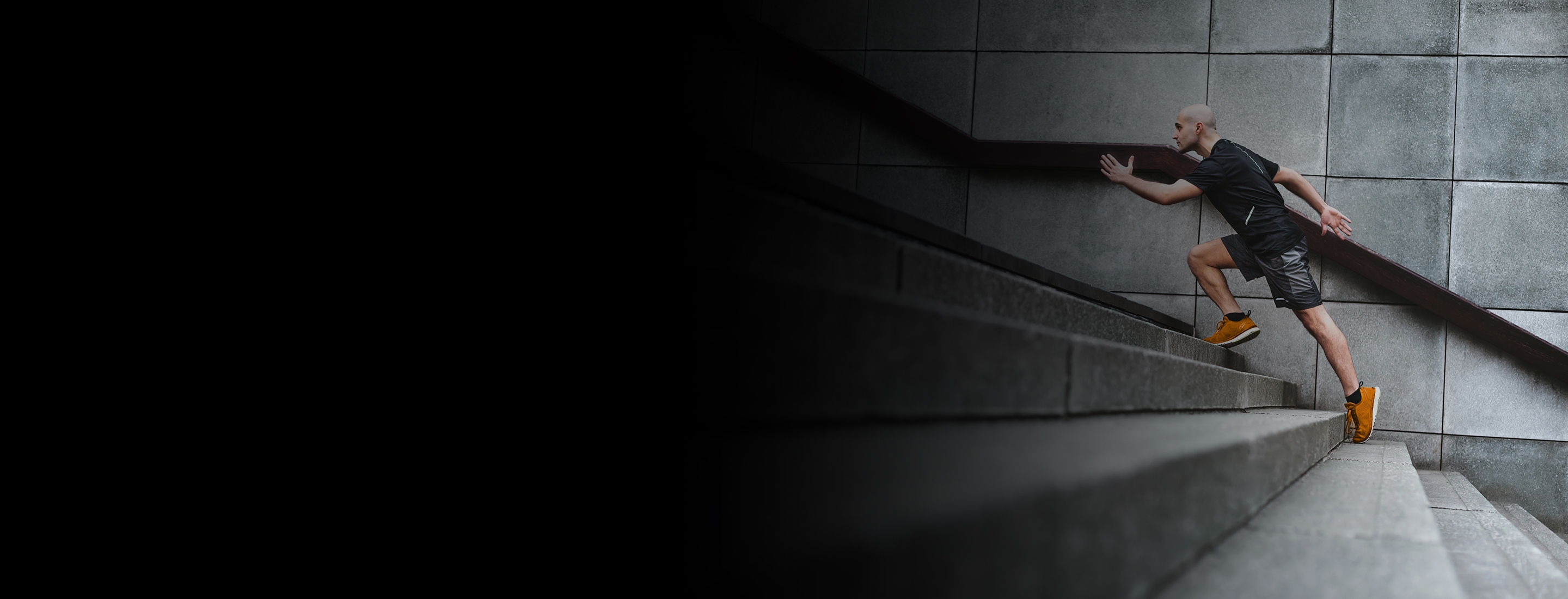 Cropped 2880x1100 left black gradient of Focussed runner man jogging on stairs