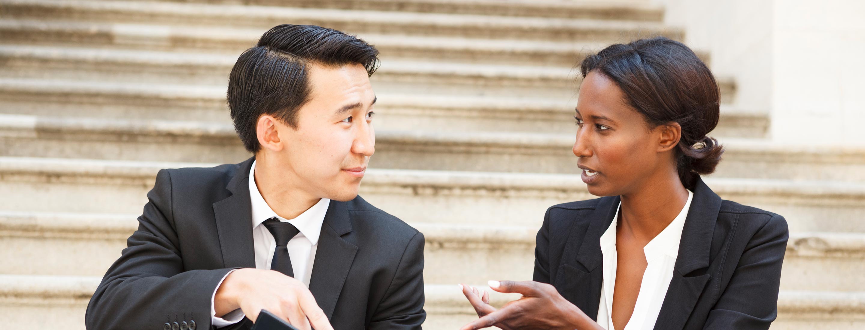 Two legal professionals sitting on steps having a conversation.