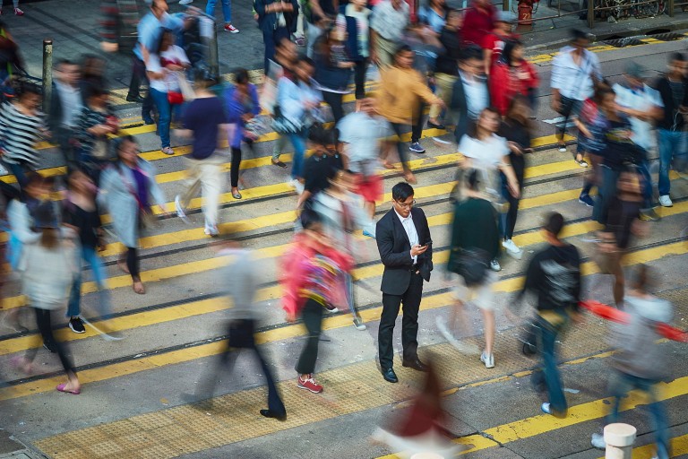High angle view of businessman using smart phone amidst crowd. Professional is standing on busy street