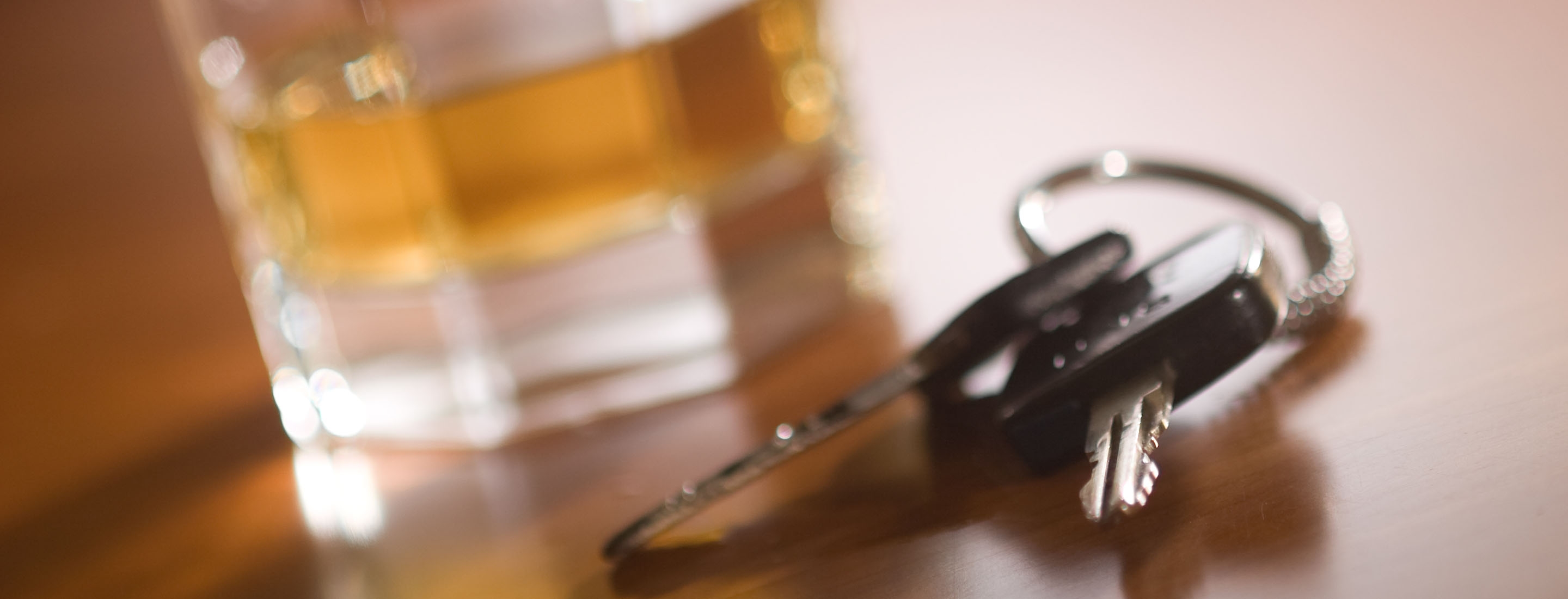 2880x1100 of a set of car keys in the foreground and glass of whiskey behind.