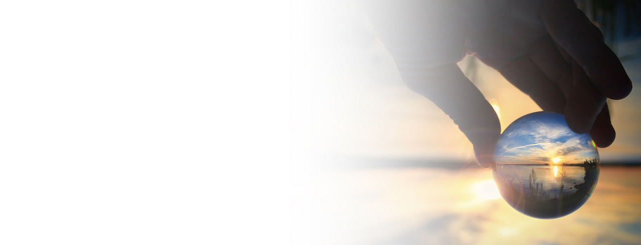 2880x1100 left white gradient flipped horizontal of fingers holding transparent glass ball reflecting the sunset on the water of a lake