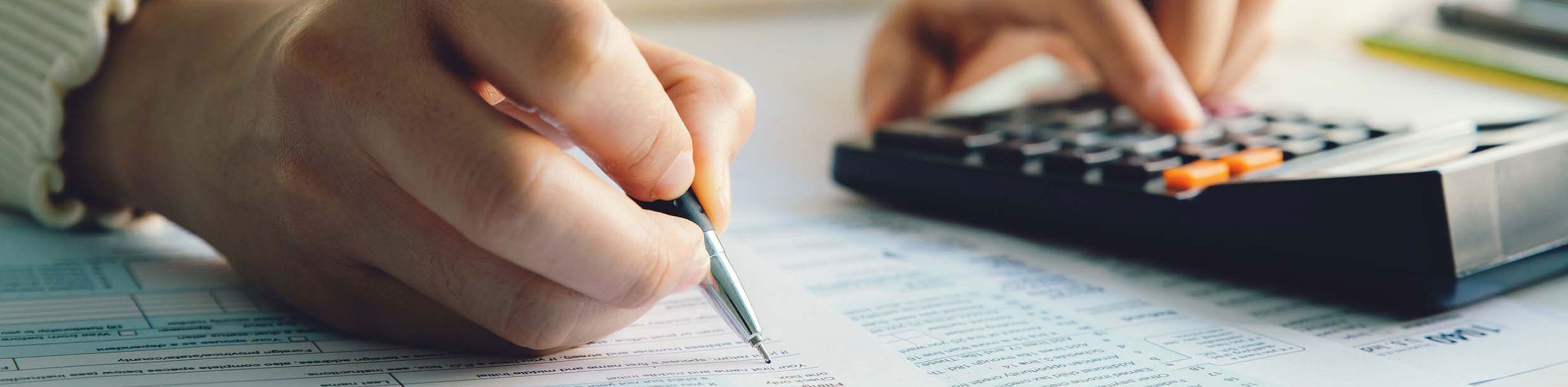 Person with pen and calculator, filling out tax forms.